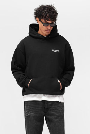Front image of a model wearing the Owners club hoodie in black, by brand Represent